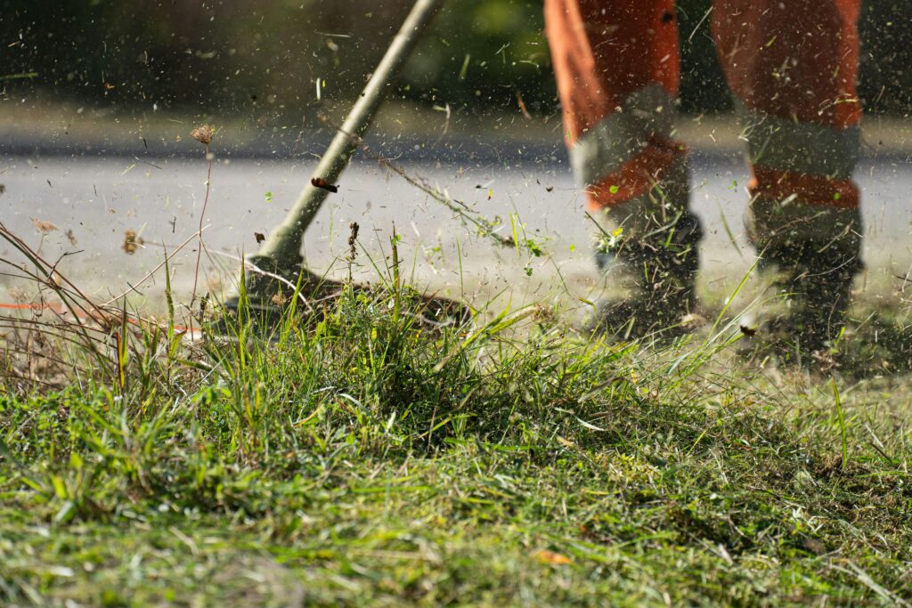 pexels photo 11400230 11400230 Close-up of a grass cutter trimming green grass with flying clippings outdoors.